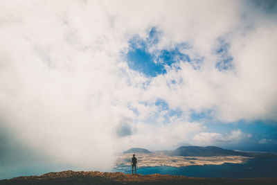 Rear view of man standing by mountain against sky