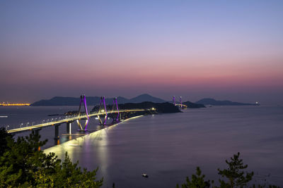 Illuminated bridge over sea against sky at sunset