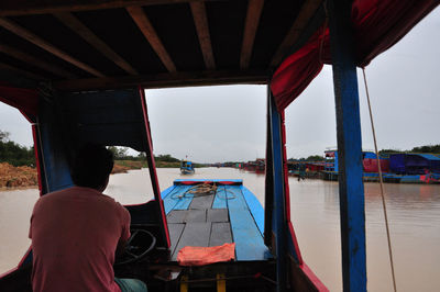 Rear view of man sitting on boat against sky