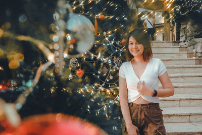 Young woman standing by christmas tree at night