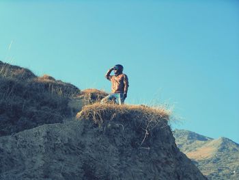 Low angle view of man standing on rock against clear blue sky