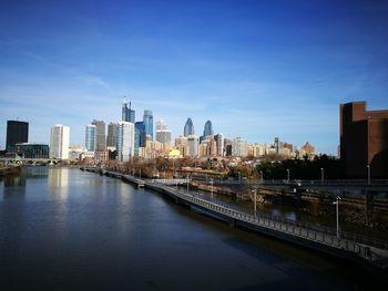 Bridge over river by buildings in city against sky