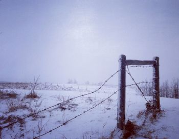 Barbed wire fence on snow field against sky