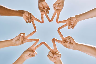 Low angle view of people holding hands against sky