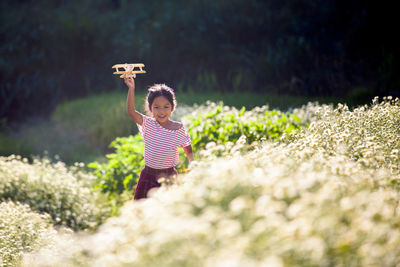 Smiling girl holding toy plane while running amidst flowers in park