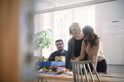 Multi-ethnic male and female engineers discussing over architectural model at table during meeting in office