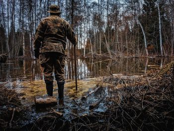 Rear view of man standing by bare trees in forest