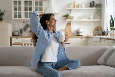 Young woman using phone while sitting on sofa at home