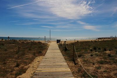 Walkway leading towards sea against sky