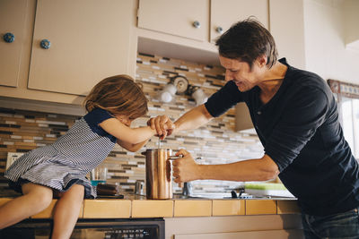 Mature father and daughter making coffee in french press at home