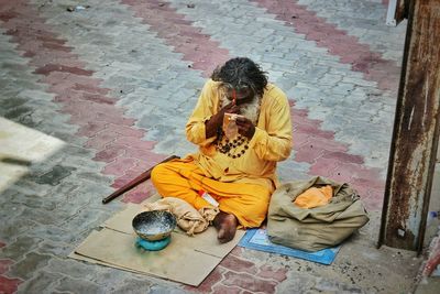 High angle view of sadhu sitting on cardboard at paved walkway