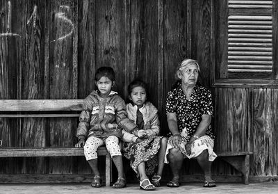 Portrait of girl sitting by sister and grandmother against house