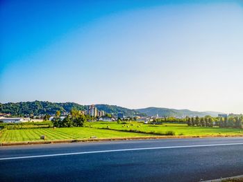 Road amidst field against clear blue sky