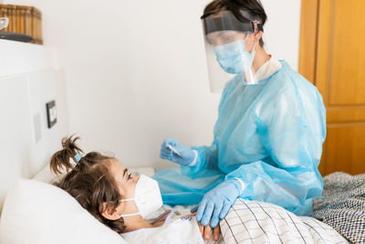 Doctor examining girl lying on bed at home