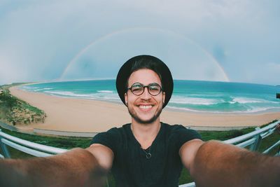 Portrait of smiling man photographing sea against sky