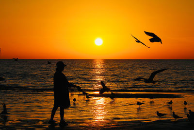 Silhouette people in sea against orange sky during sunset