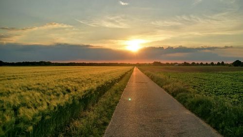 Road amidst agricultural field against sky during sunset