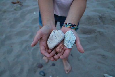 Low section of woman holding pebbles at sandy beach