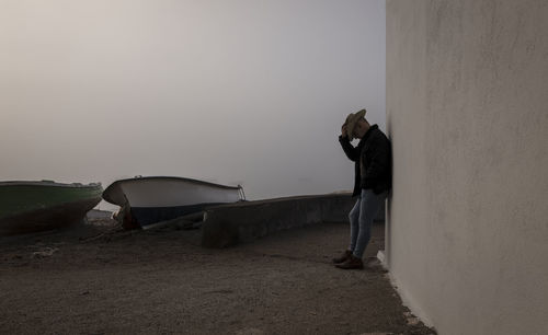 Portrait of adult man in cowboy hat and jeans against wall with fishing boat in background. almeria