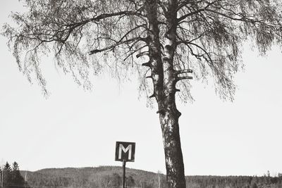 Road sign by tree on field against clear sky