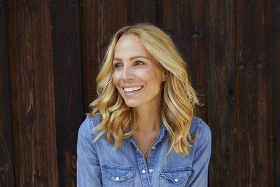 Happy blond woman in front of wooden wall