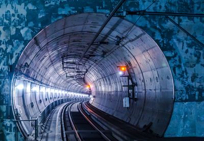 Railroad tracks leading to illuminated tunnel at night