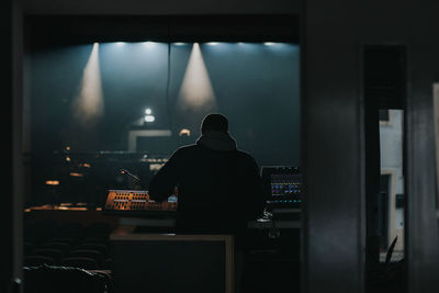 Rear view of man sitting on table in illuminated room