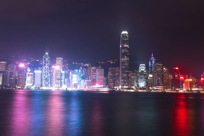 Illuminated buildings by river against sky at night