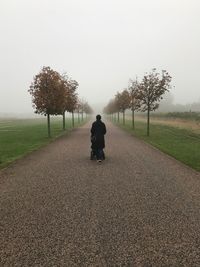 Rear view of woman with baby carriage walking on road in foggy weather