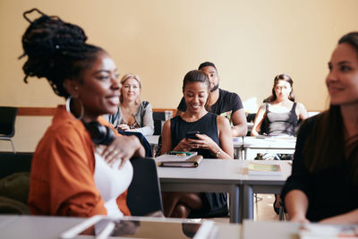 Mature woman using smart phone while sitting with classmates in language class