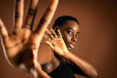Black female model with short hair looking at camera and making protective gesture against brown background