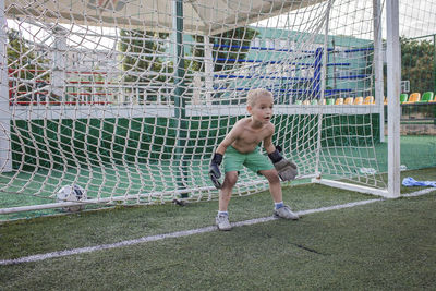 Full length of shirtless boy playing soccer on land