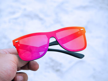 Close-up of hand holding sunglasses against sky