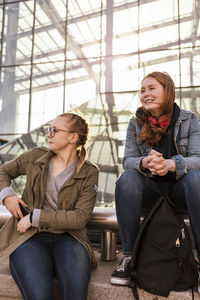 Teenage girls sitting against modern building in city