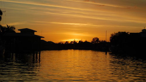 Silhouette buildings by lake against sky during sunset