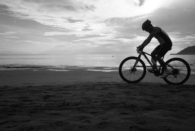 Man riding bicycle on beach against sky