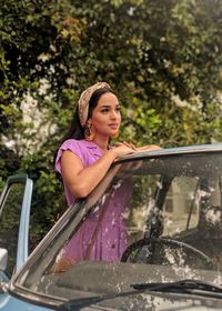 Young woman looking away while standing by car