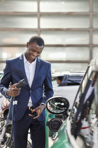 Happy businessman holding electric plug at vehicle charging station