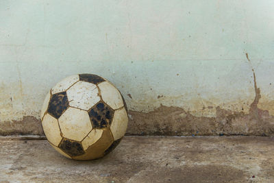 Close-up of abandoned soccer ball on footpath against wall