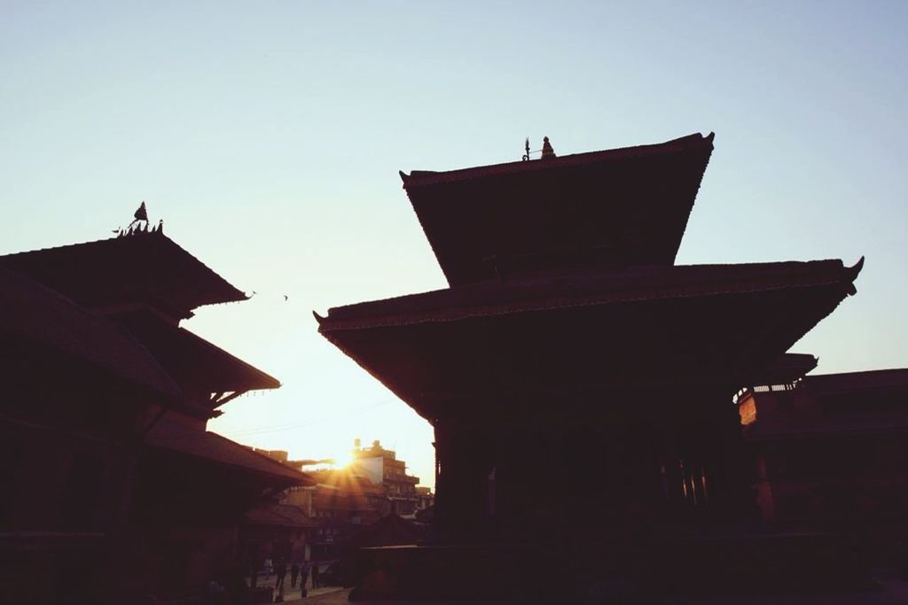 building exterior, architecture, built structure, sunset, clear sky, sun, low angle view, sunlight, sky, silhouette, place of worship, copy space, religion, house, outdoors, spirituality, city, no people, sunbeam, church