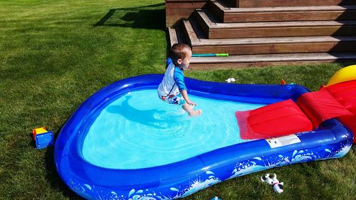 High angle view of boy jumping in wading pool at backyard