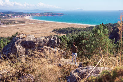 Rear view of man standing by sea against sky