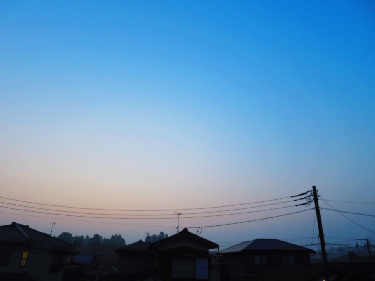 SILHOUETTE HOUSES AND ELECTRICITY PYLON AGAINST CLEAR SKY