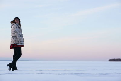 Side view of transgender male walking on snowfield against sky during sunset