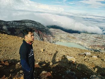 Young man standing on rock against sky