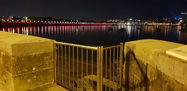 High angle view of illuminated city by river against sky at night