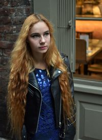 Portrait of young woman standing against brick wall