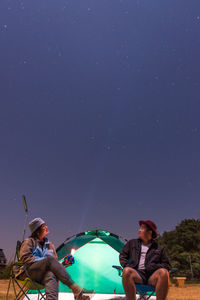 Men sitting against sky at night