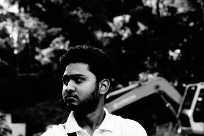 Serious man with beard looking away against trees