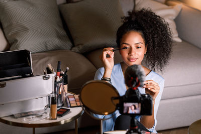 Camera filming young woman applying beauty product while sitting at home